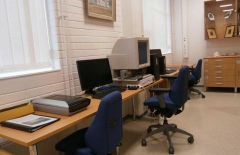 Mikrofilminlukulaite, tietokone ja skanneri pöydällä sekä kaksi tuolia kotiseutuhuoneessa