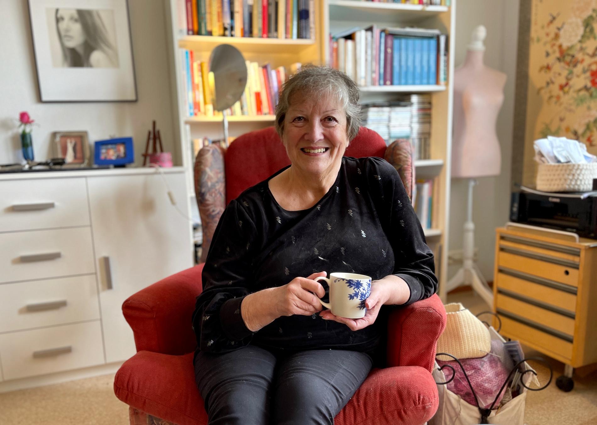 A smiling woman sitting home with a cup of coffee in her hand.